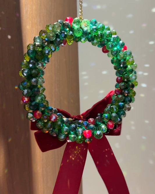 A finished beaded Christmas wreath with green glass beads and a red velvet bow hanging on a wooden door.
