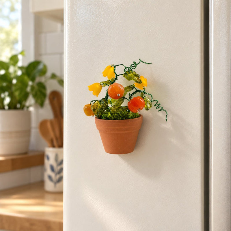 The Pumpkin Garden beaded magnet displayed on a refrigerator, with orange pumpkins, yellow flowers and green leaves.