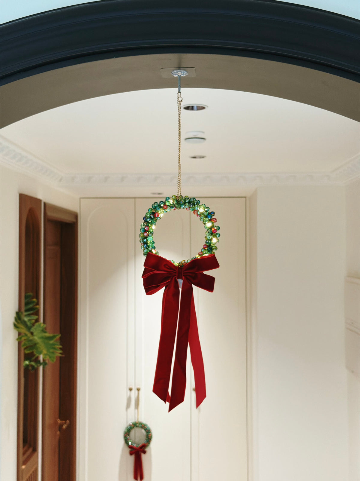 Beaded Christmas wreath ornament with a red velvet bow, handmade from glass beads, hanging on a Christmas tree