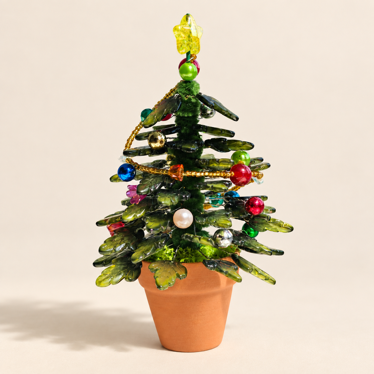 Dark green beaded Christmas tree with colorful ornaments and terracotta pot on a milk-tea beige background