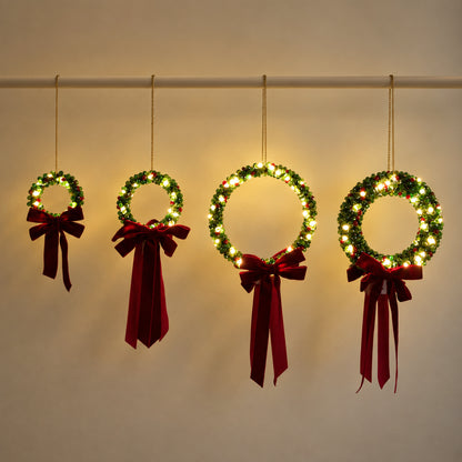 Four illuminated beaded Christmas wreaths hanging side by side from a single rod, showing their different sizes and ring thicknesses.