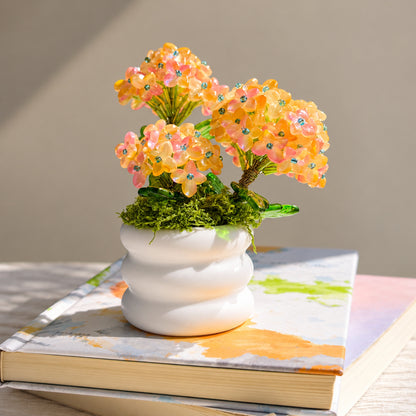 Beaded hydrangea flowers with green leaves in a white ceramic pot on a book.