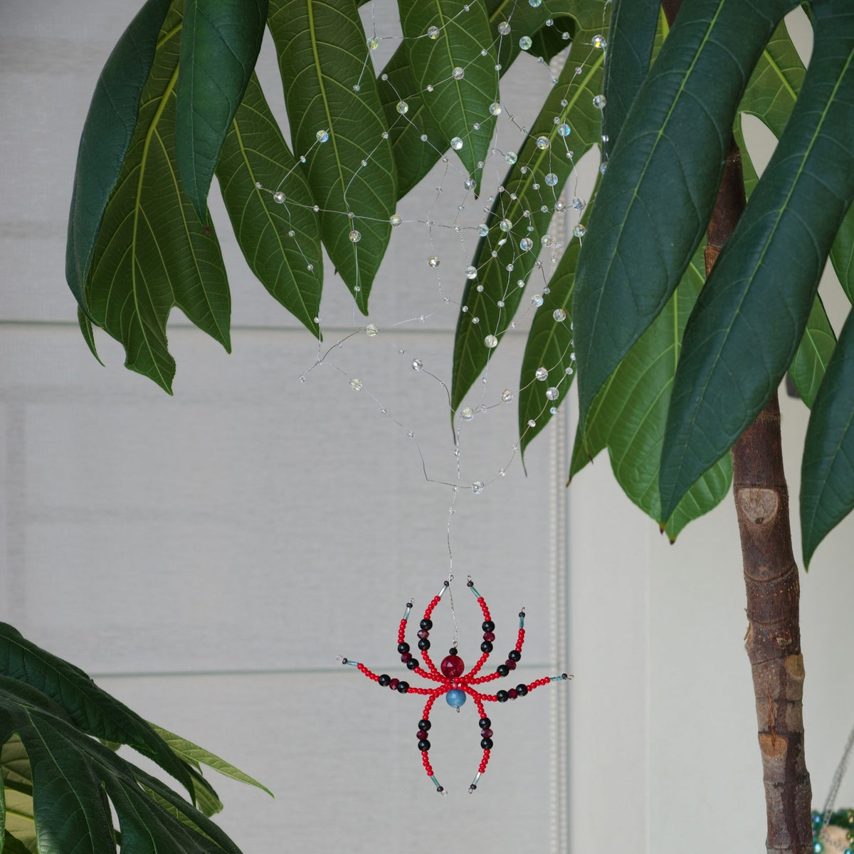 Real photograph of a clear beaded spider web and red and black spider hanging among green leaves