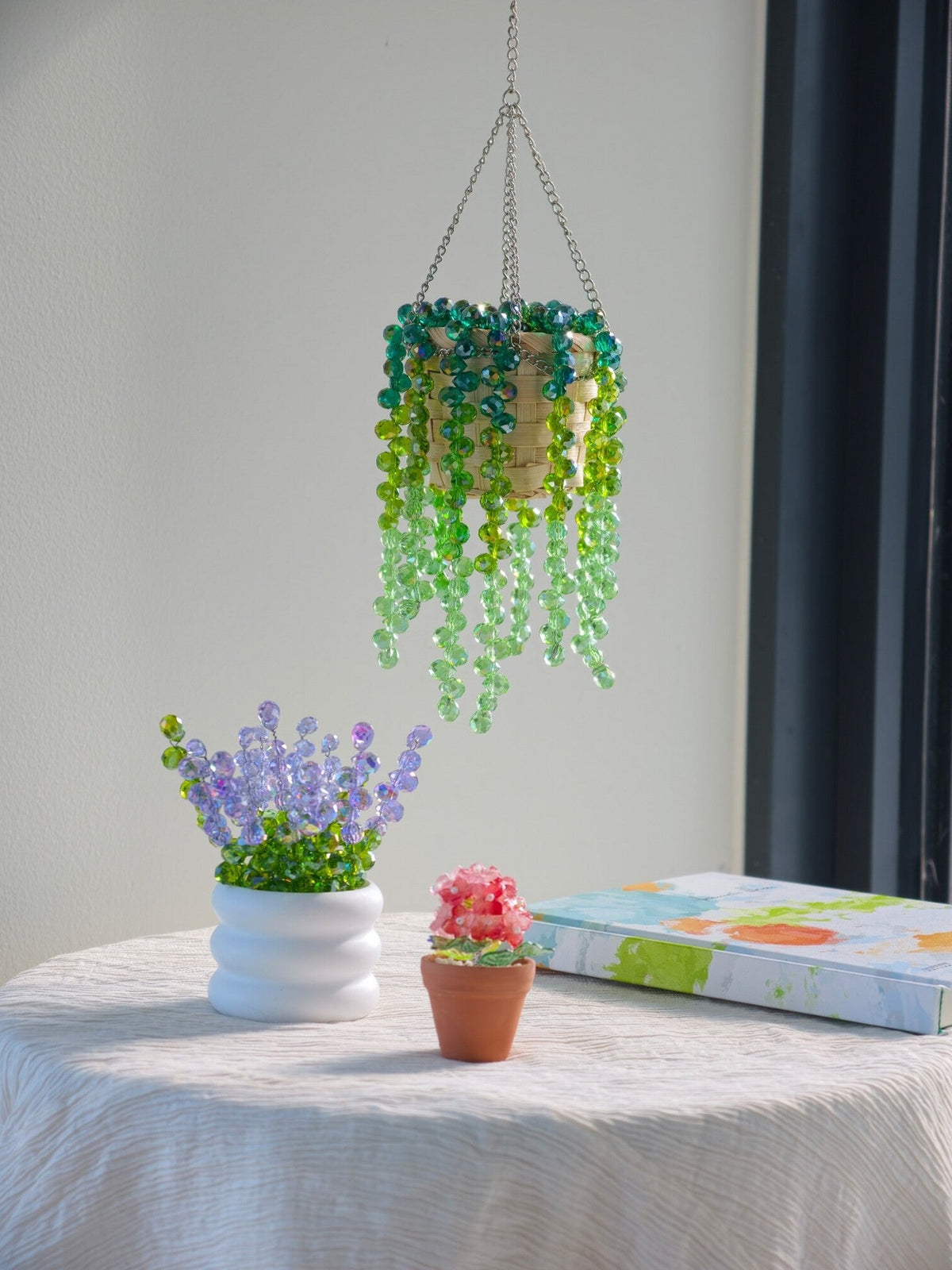 Beginner beading collection styled together: green hanging beaded plant, a white pot of lavender beads and a mini potted beaded plant, with the kit box