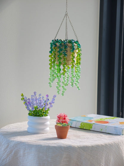 Beginner beading collection styled together: green hanging beaded plant, a white pot of lavender beads and a mini potted beaded plant, with the kit box