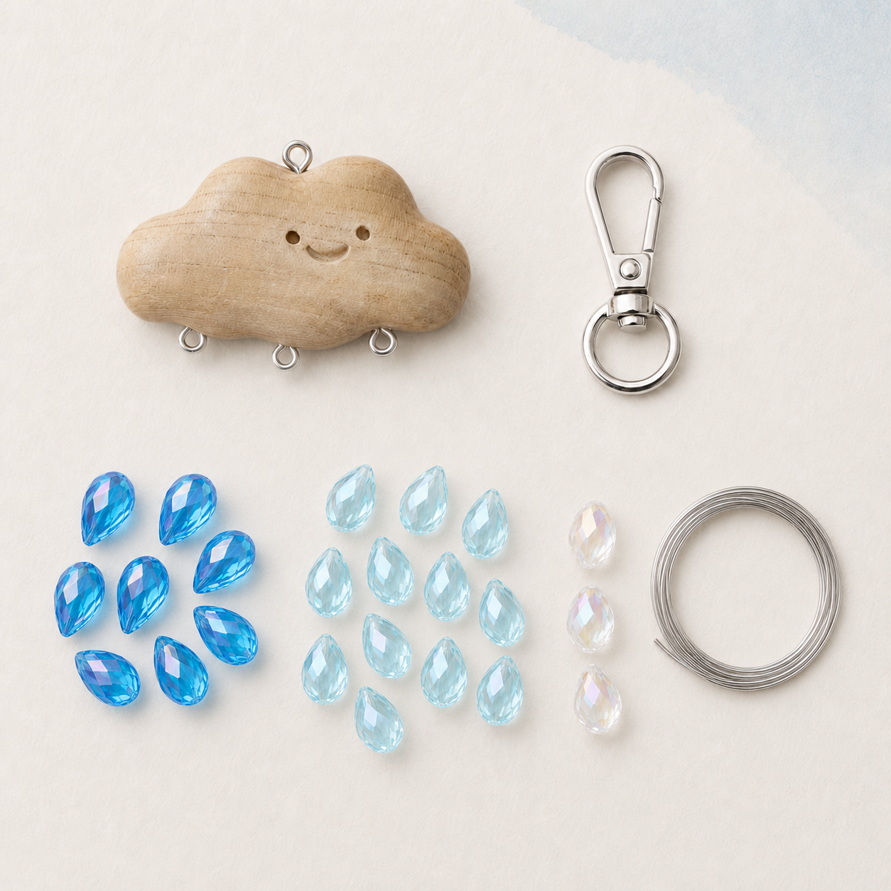 Cloud charm DIY kit with deep lake-blue, light lake-blue, and transparent AB teardrop glass beads, wooden cloud connector, silver lobster clasp, and coiled steel wire
