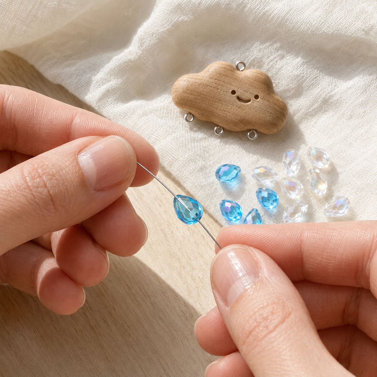 Hands threading a blue faceted teardrop glass bead onto silver wire to make a cloud rain charm