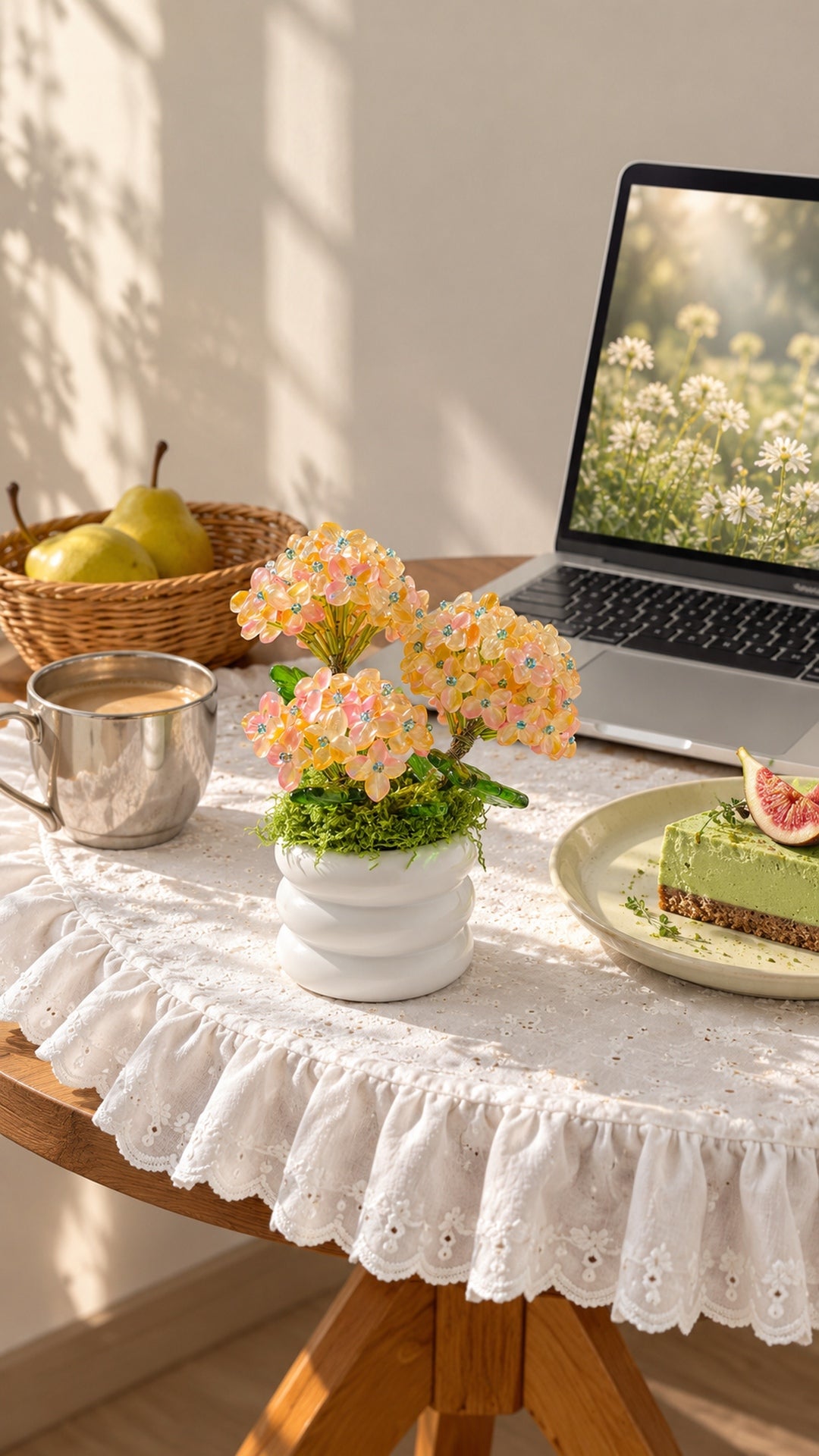 Pink and yellow beaded hydrangea on a lace-covered table beside a laptop, tea and cake.