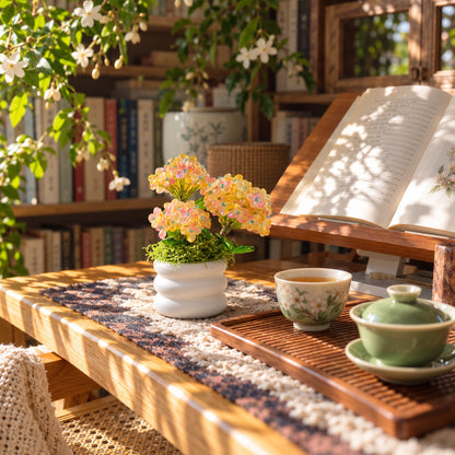 Miniature beaded hydrangea arrangement on a wooden study table beside tea and an open book.