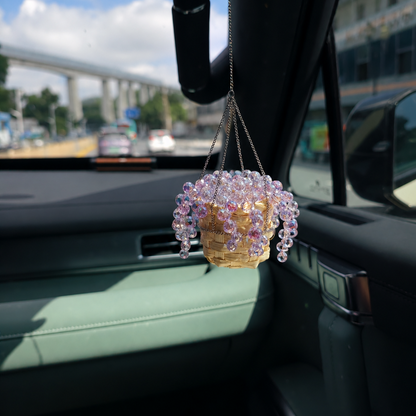 A small hanging beaded basket ornament with iridescent purple beads and a silver craft wire, suspended inside a car near the windshield.