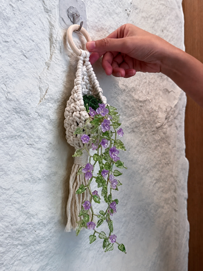 Hand adjusting a flower vine beaded wall hanging with purple blooms on a white stone wall
