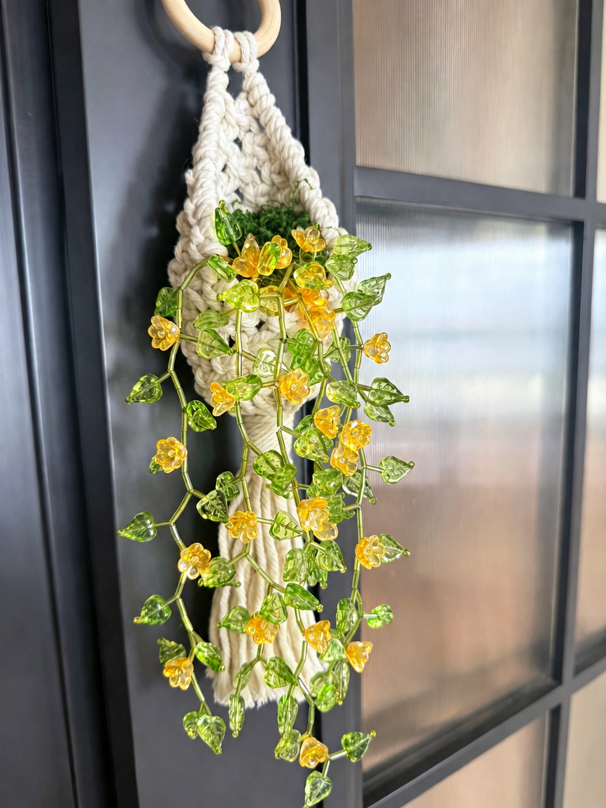 Flower vine beaded wall hanging with yellow blooms and green leaves on a dark window