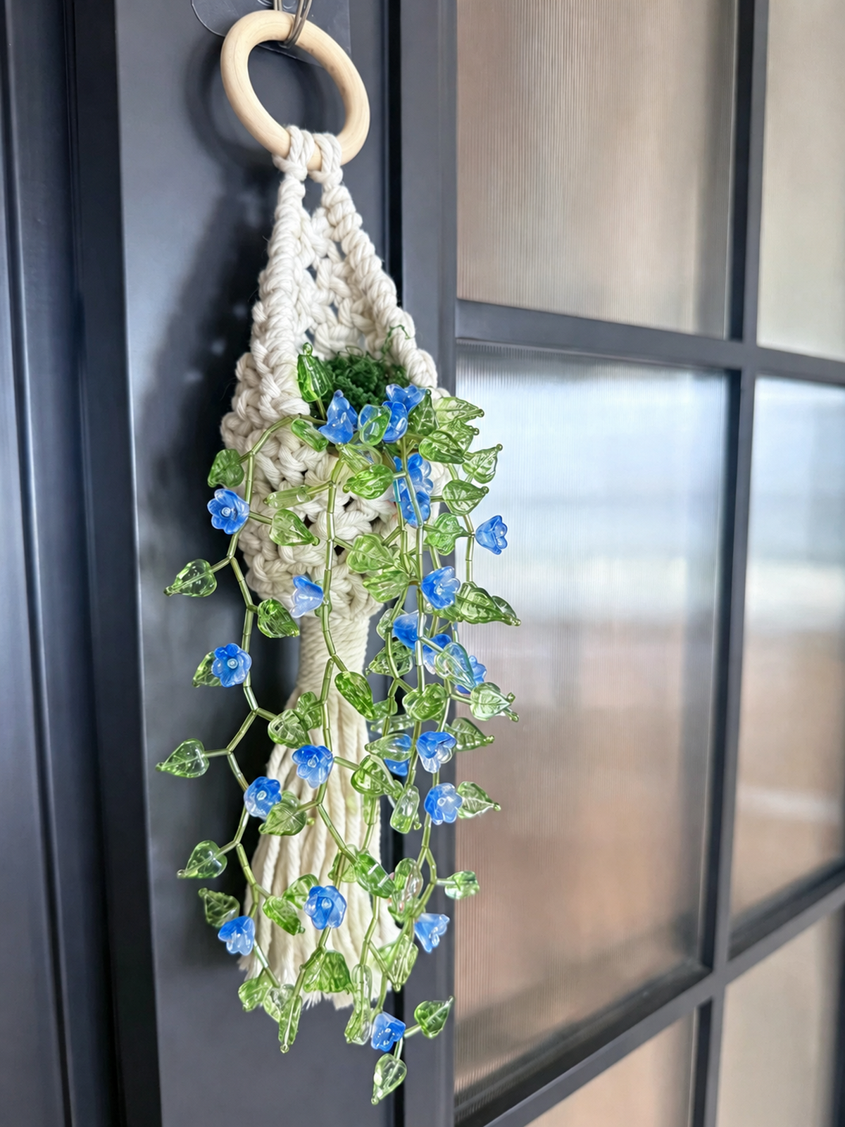 Flower vine beaded wall hanging with blue blooms and green leaves on a dark window frame