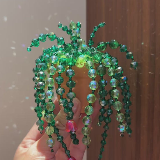 Hand holding an enchanted garden beaded plant with emerald green strands and pink bead accents