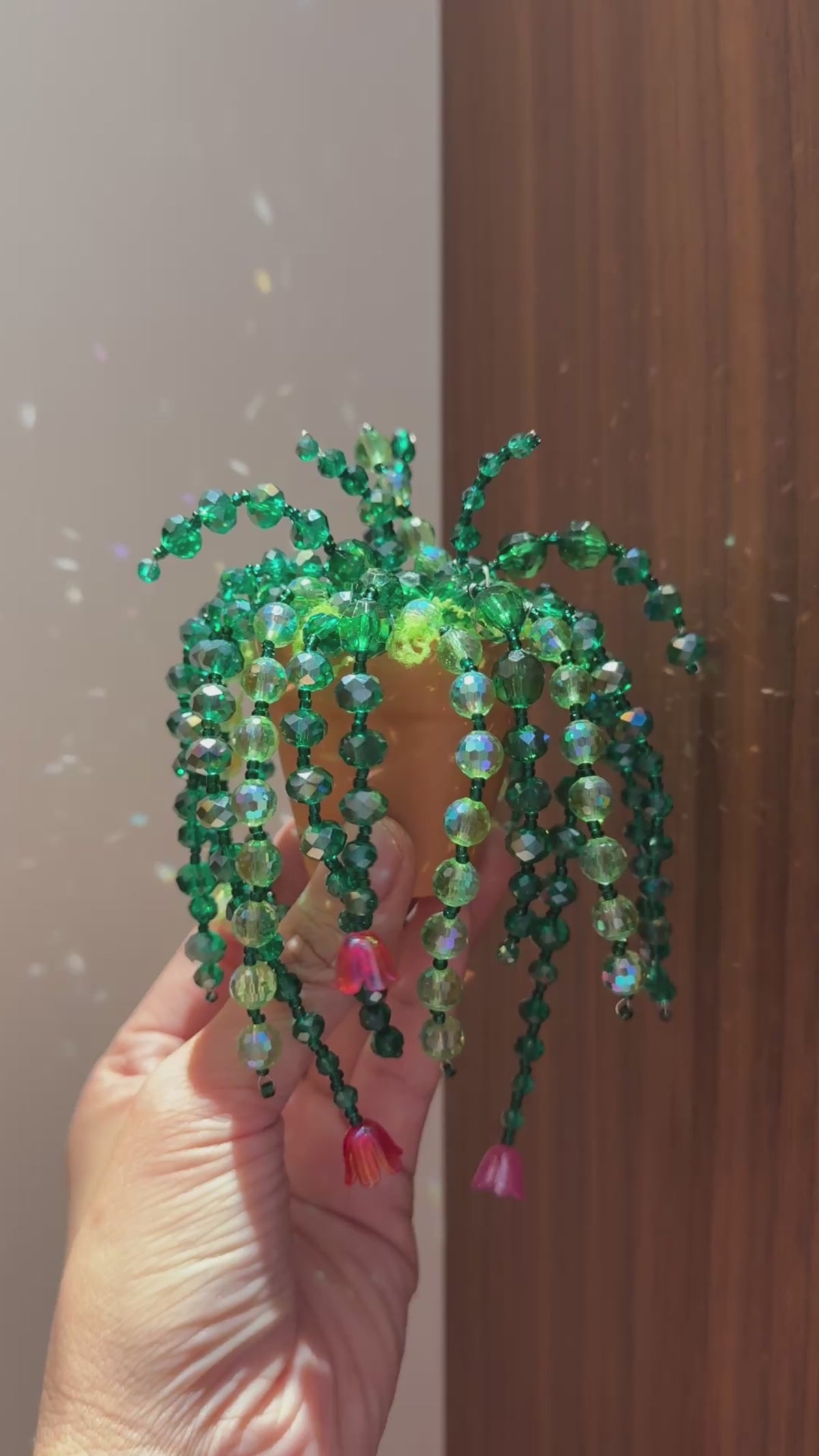 Hand holding an enchanted garden beaded plant with emerald green strands and pink bead accents