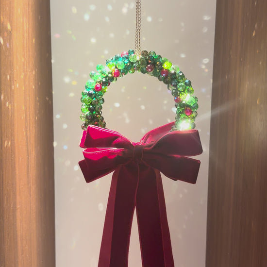 Beaded Christmas wreath glowing with warm fairy lights, finished with a burgundy velvet bow