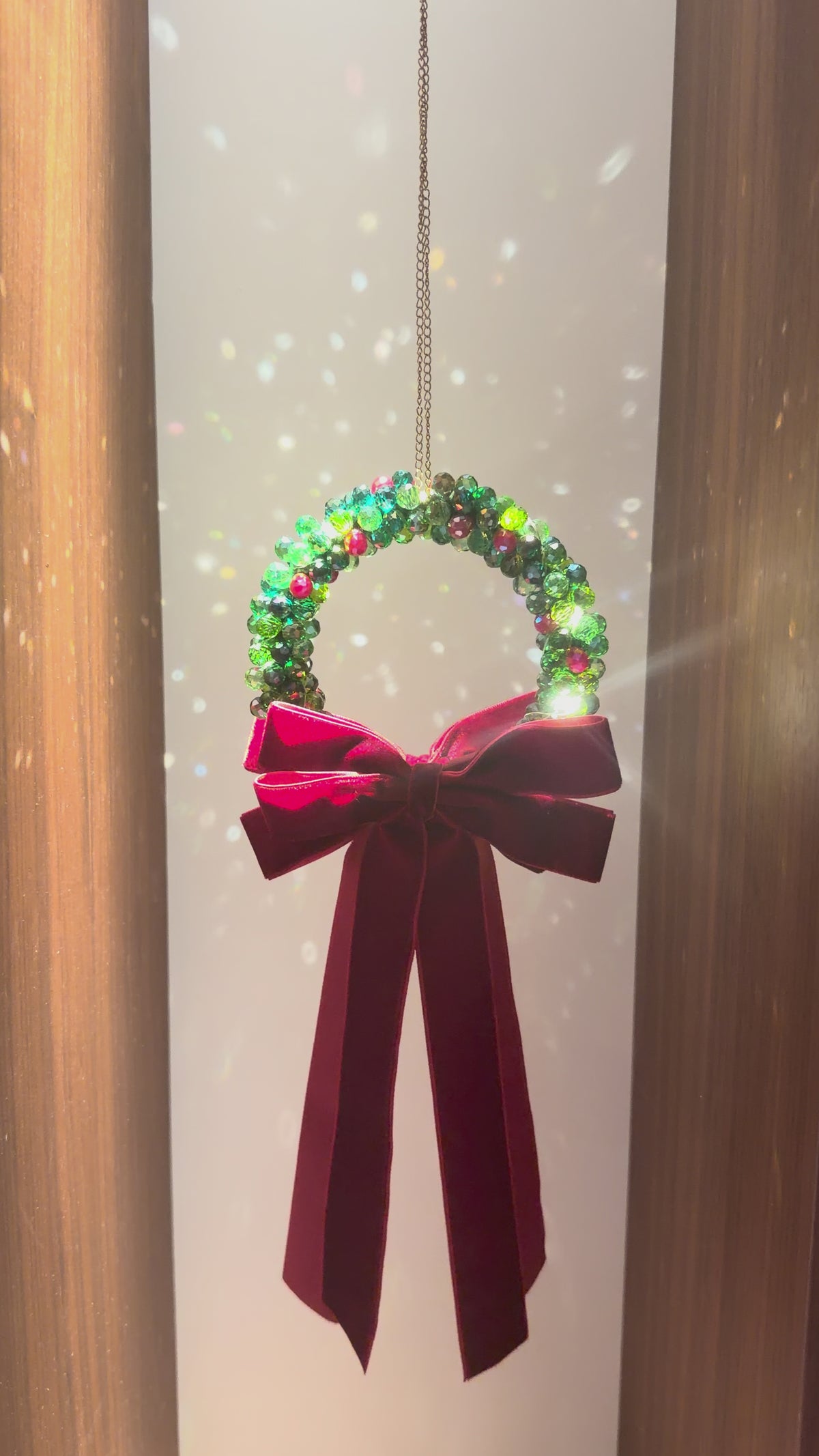 Beaded Christmas wreath glowing with warm fairy lights, finished with a burgundy velvet bow