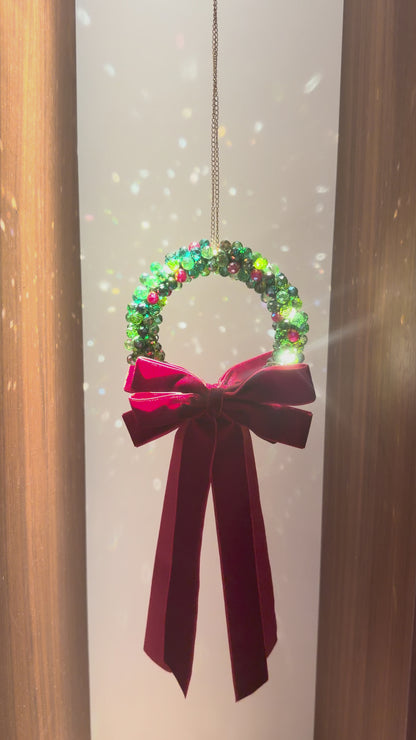 Beaded Christmas wreath glowing with warm fairy lights, finished with a burgundy velvet bow
