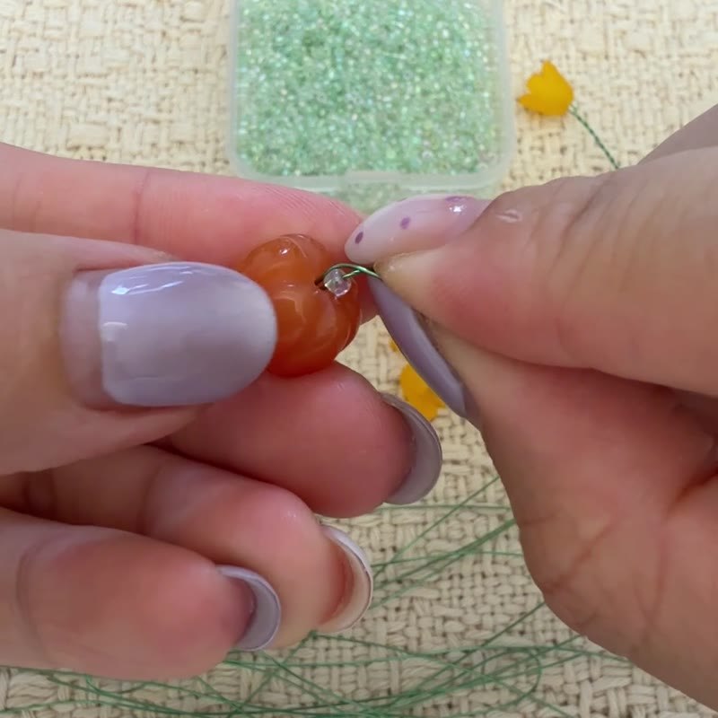 A pumpkin held between seed beads on wire.