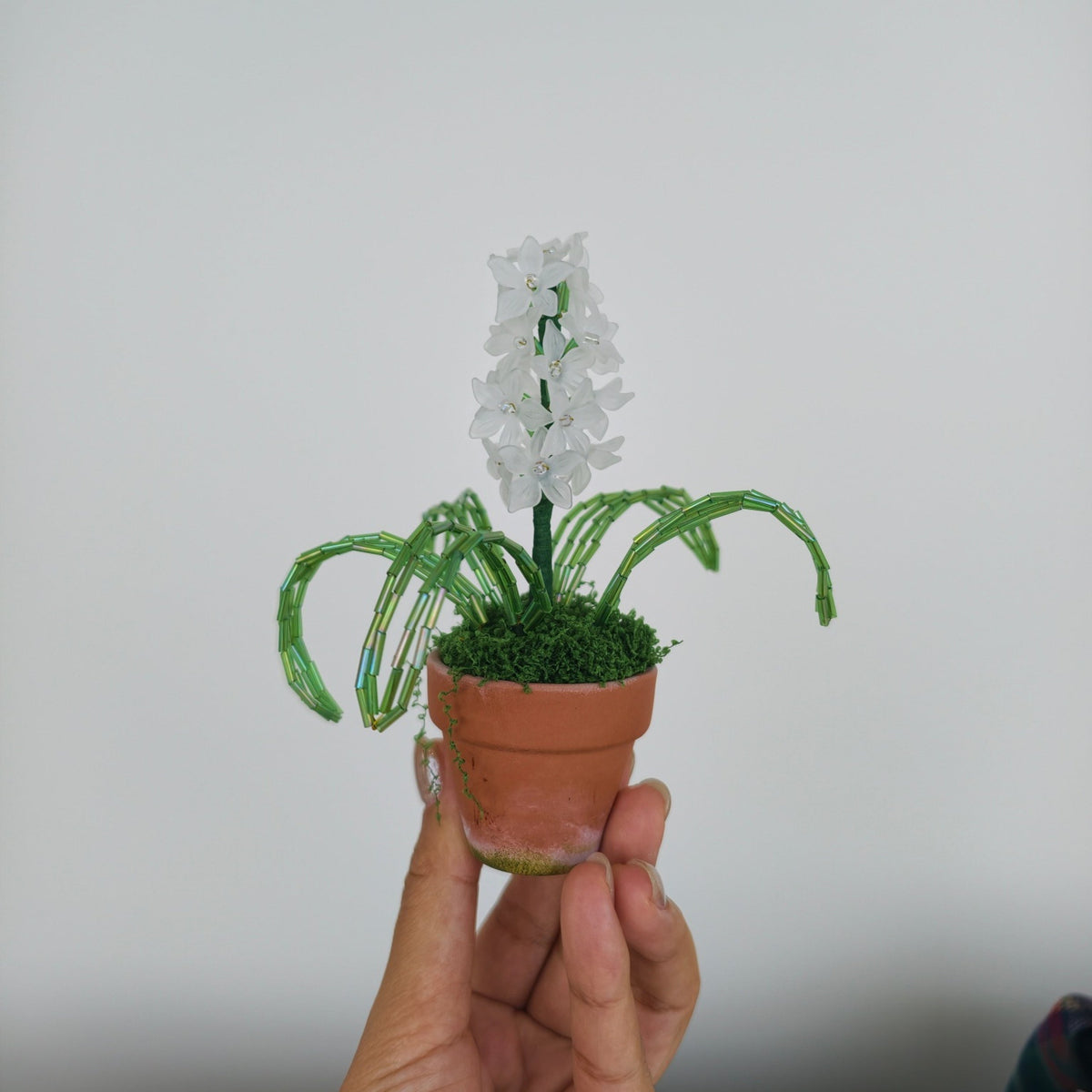 Original side view of the handmade white beaded hyacinth held in a hand for scale.