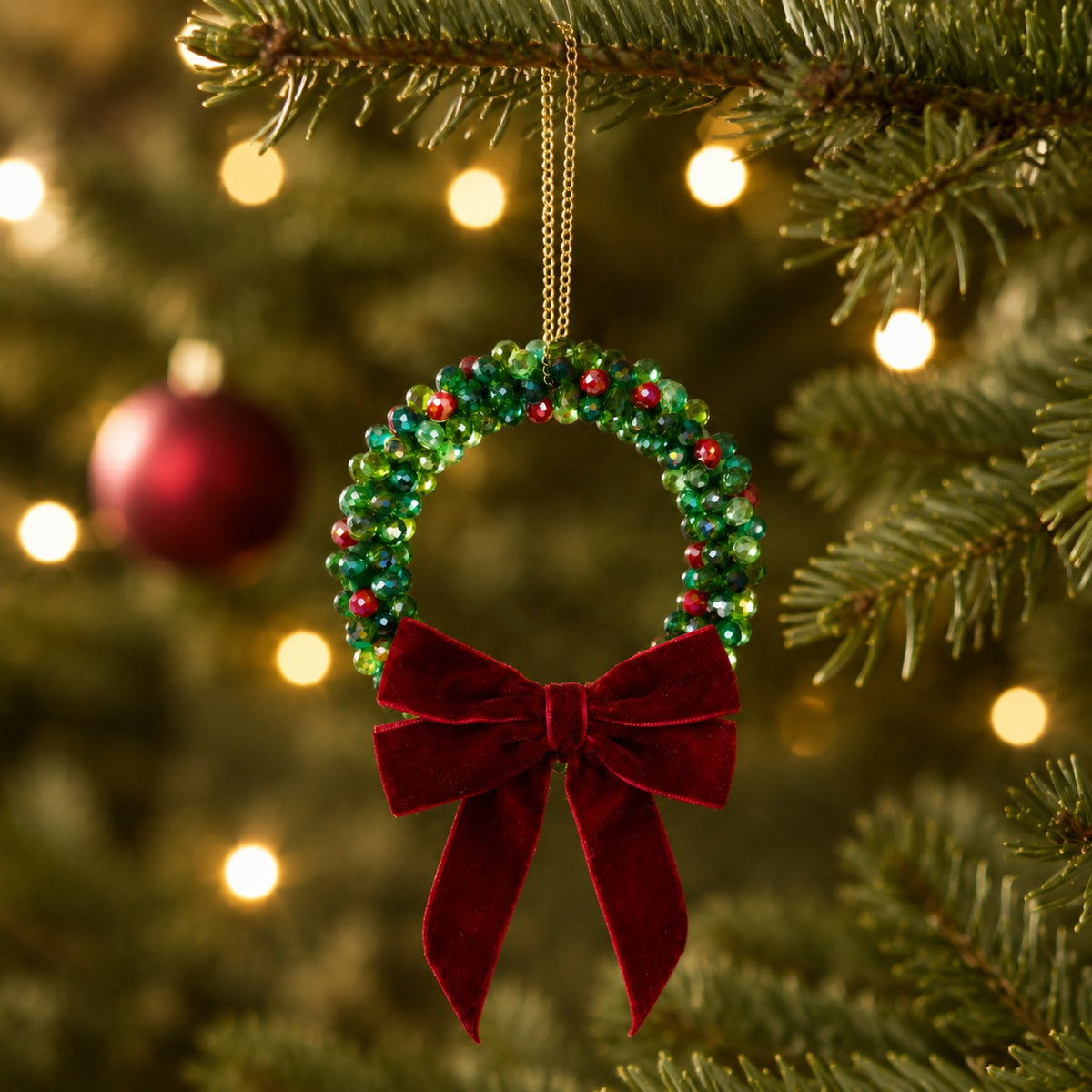 Beaded Christmas wreath ornament with a red velvet bow, handmade from glass beads, hanging on a Christmas tree